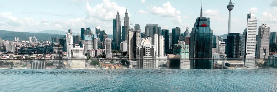 Skyline view of Kuala Lumpur with a rooftop pool in the foreground and iconic towers in the background under a partly cloudy sky