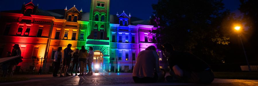 groups of students at night outside of University Hall lit up with a variety of colors