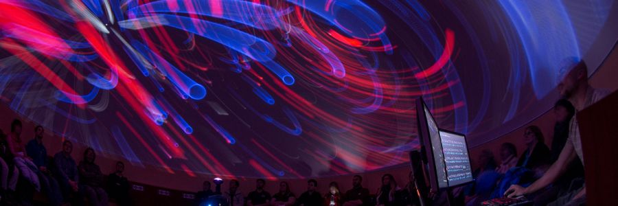 circle of people in a dark room looking up at a planetarium ceiling with colors and shapes swirling around