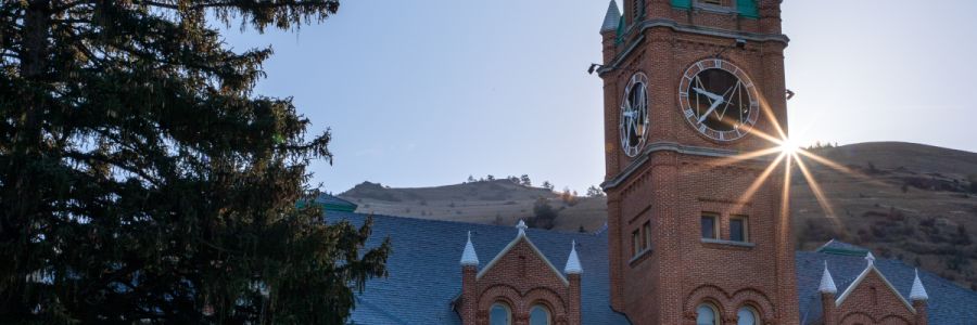 University Hall clock tower seen from below with sun coming shining from behind