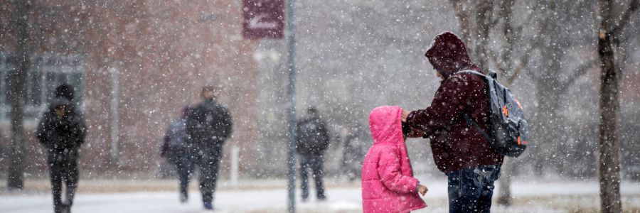 parent adjusting childs coat while they stand outside in the snow on the UM campus