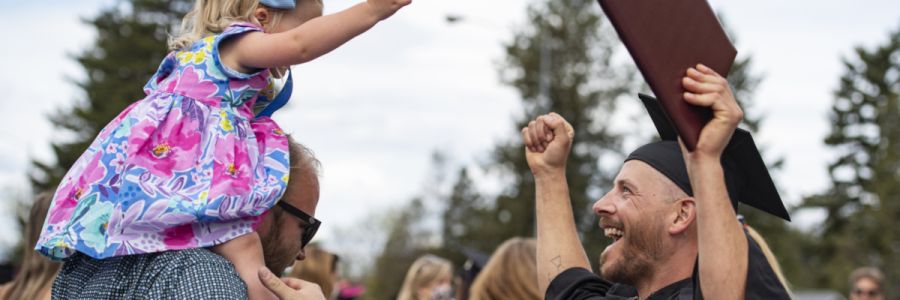 man holding child on his shoulders celebrating with another person in graduation garb