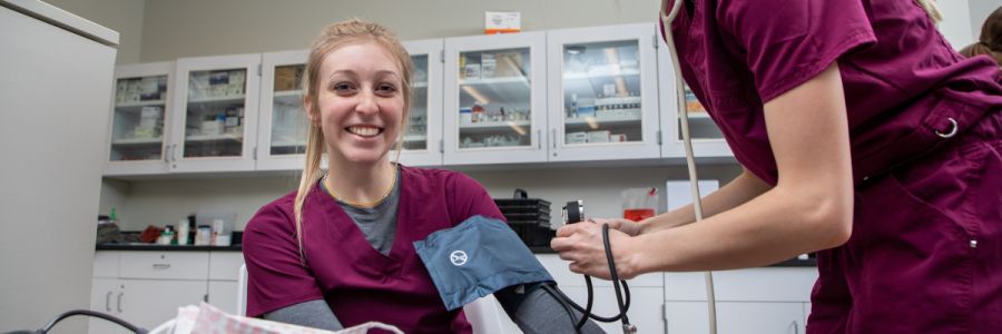 student nurse smiling while being given a blood pressure test by another nurse