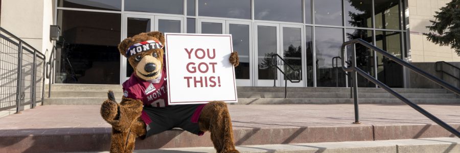 UM mascot Monte holding a You Got This sign while sitting on steps outside