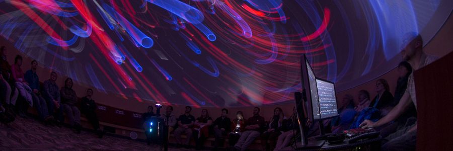 group of students looking at swirling colors and shapes on the ceiling of a planetarium