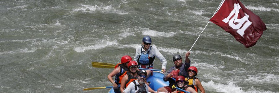 group of people on a raft floating down a river waving the UM flag