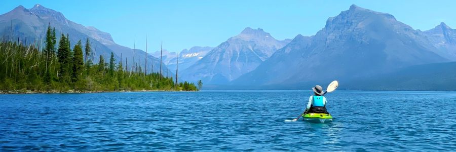 A paddler kayaks across a lake in the mountains