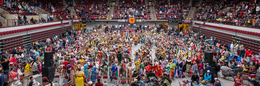 large group of people in traditional Native American clothing in the Adams Center
