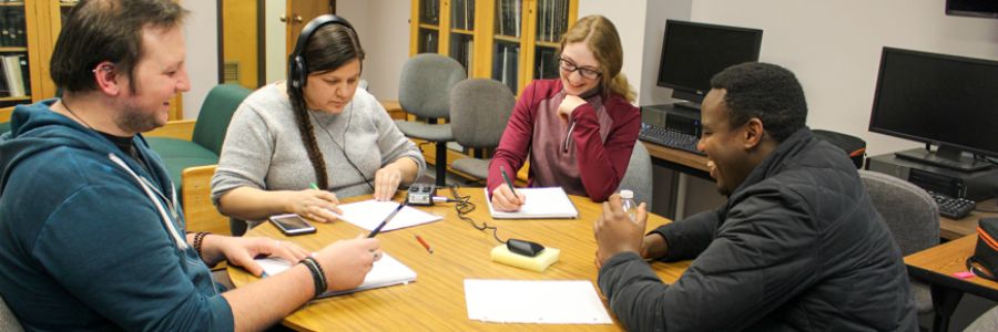 four students sitting around a table listening to each other and taking notes