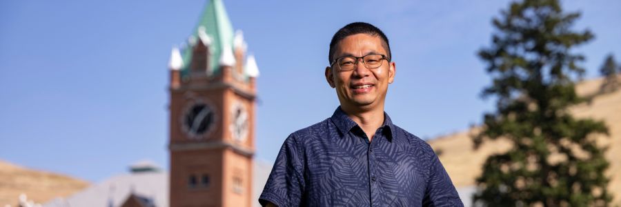 Lu Hu standing on the UM oval on a sunny day with University Hall in the background