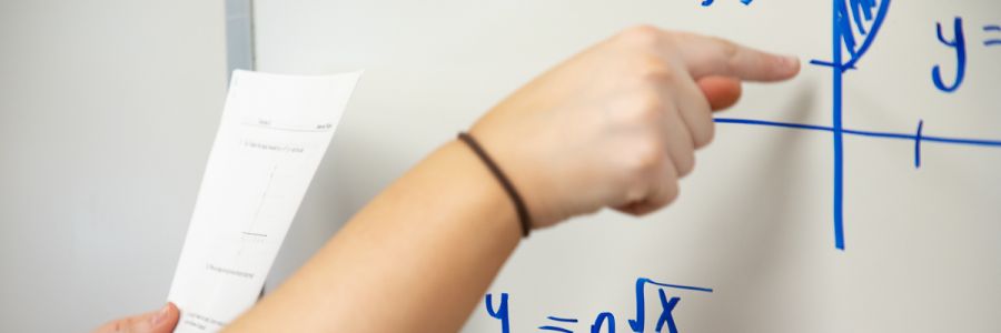 close up of a hand pointing at an equation written on a white board