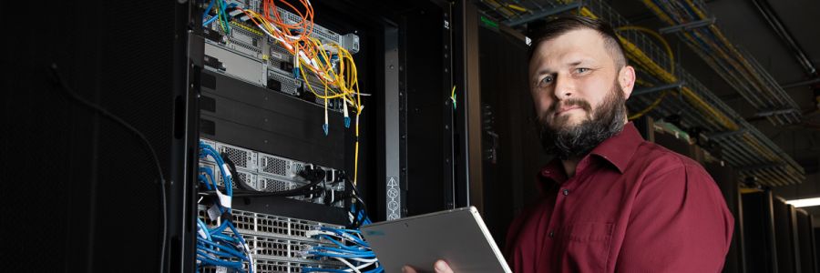 computer technician standing with a tablet next to an open server rack 