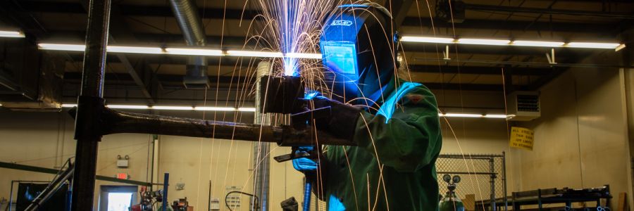 person wearing a welding mask while welding with sparks flying from the metal