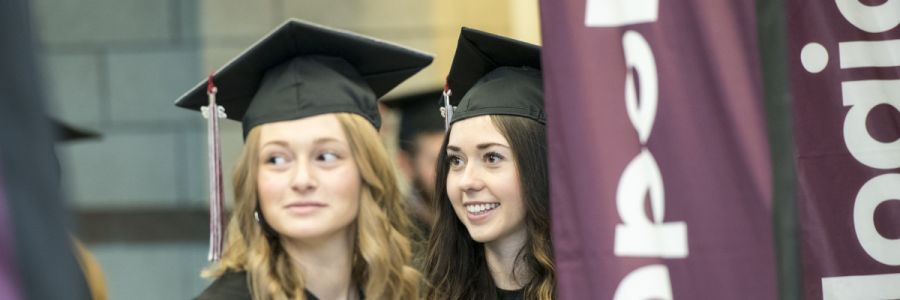 two students in graduation garb smiling and looking to the left out of the image