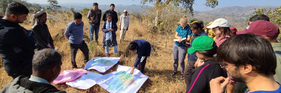 group of people on top of a hill viewing several paper maps laid out on the ground