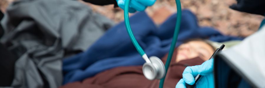end of a stethoscope in the foreground with a patient lying on the ground in the background