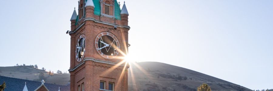 University Hall clock tower seen from below with sun shining from behind