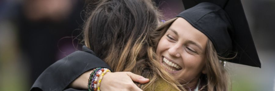 smiling student in graduation clothing hugging another person