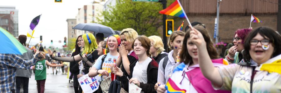 row of people at a parade holding rainbow and other colored flags 