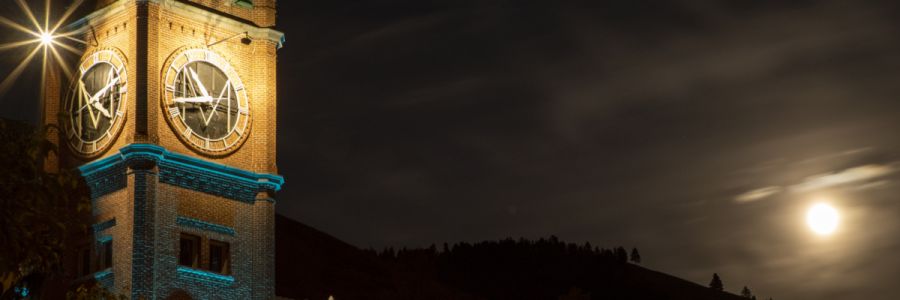 University Hall clock tower lit up at night with the full moon shining on the right