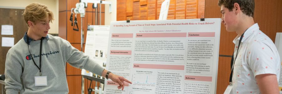 student pointing at an informational poster while talking to another student
