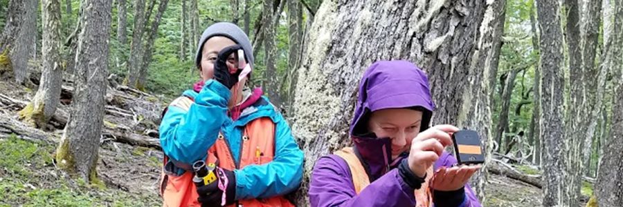 two people in rain coats looking through tools in a forest