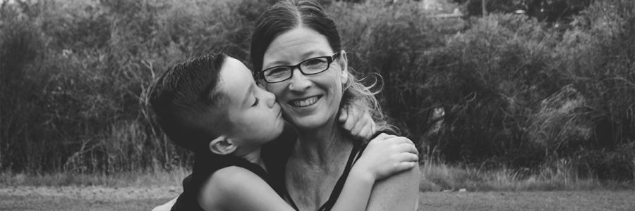child kissing a woman on the cheek while sitting outside