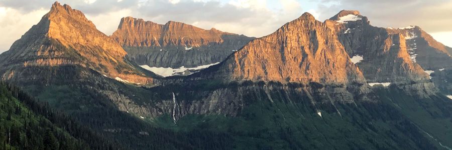 tall rocky mountains with scattered snow in orange sunlight