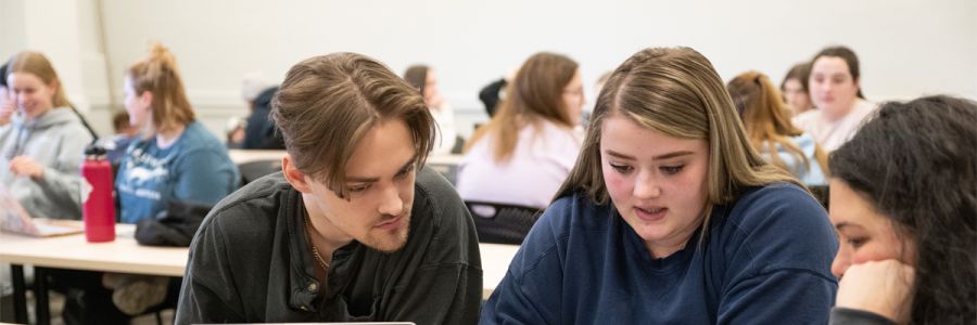 classroom full of students working in groups with a group of three talking in the foreground