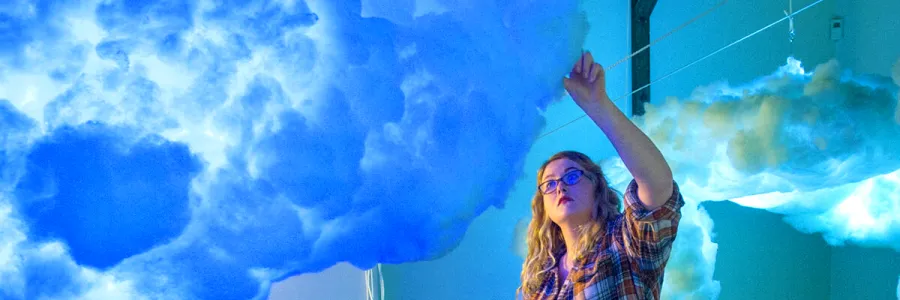 A UM School of Visual and Media Arts student adjusts a hanging cloud piece before an art gallery show.