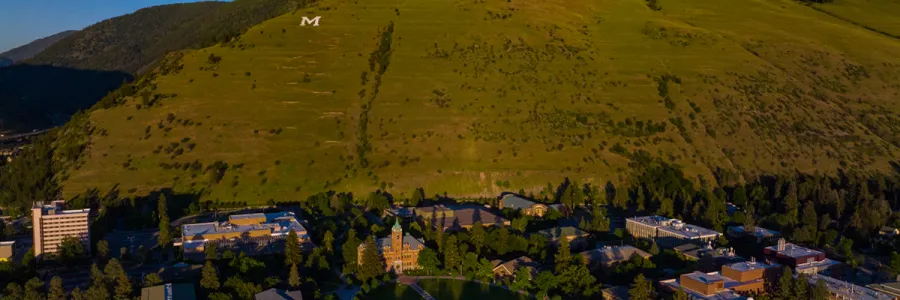 Aerial view of the 91Ԫ campus in Missoula, MT on a sunny day with blue sky and Mt. Sentinel and the M trail in the background.