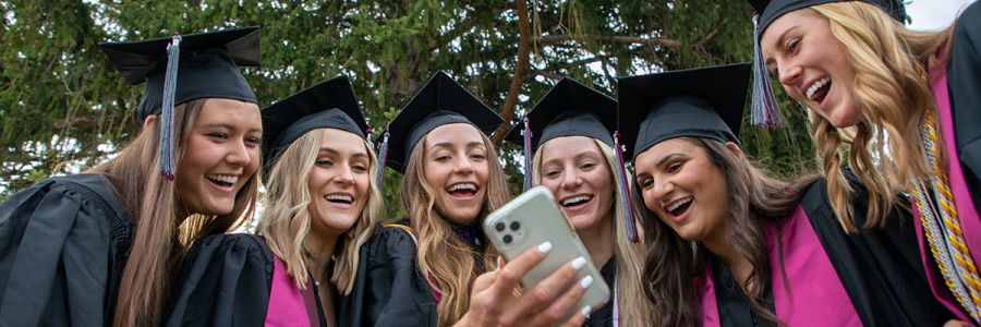 group of students in graduation garb looking at a cell phone
