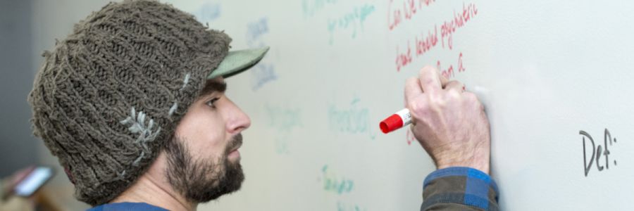 student writing on a whiteboard with a red marker