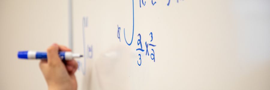 closeup view of a hand writing equations on a white board