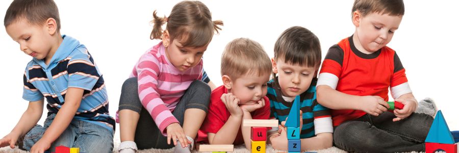 five toddlers sitting in a row playing with blocks