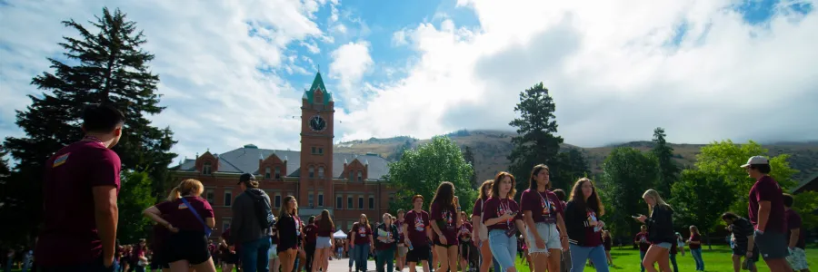 large group of students in griz colors walking along a path on the UM campus