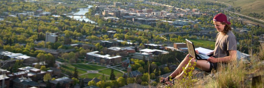 student working on their laptop at the top of the M trail overlooking campus and Missoula