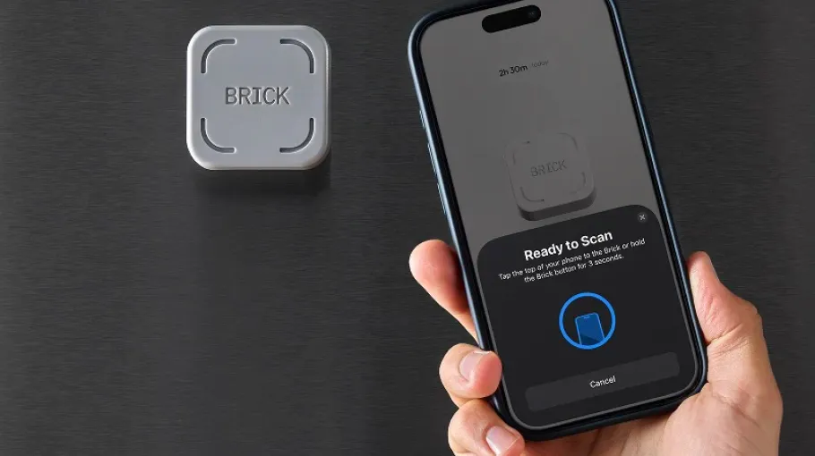 A hand holds a cell phone with text on the screen that reads 'Ready to Scan.' A Brick device is mounted on the surface next to the phone.