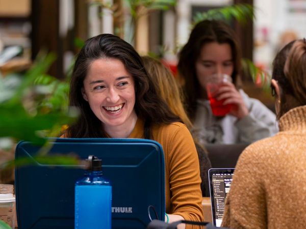 Two women engaged in work, sitting at a table with laptops open, focused on their tasks.