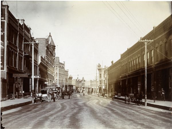 Front Street in Missoula, �����ؿ� looking west towards Higgins Avenue. The Missoula Mercantile building can be seen on the right. In the foreground are the Missoula Steam Laundry and Rankin Hotel. A horse-drawn coach with a Rankin Hotel sign waits in front of the hotel building. Several horse-drawn buggies are parked on the sides of the street. Pedestrians can be seen on the sidewalk. 