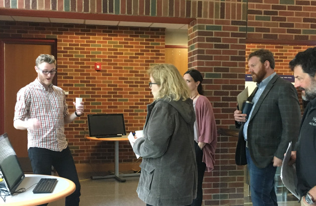 Faculty members gather around a student who is presenting