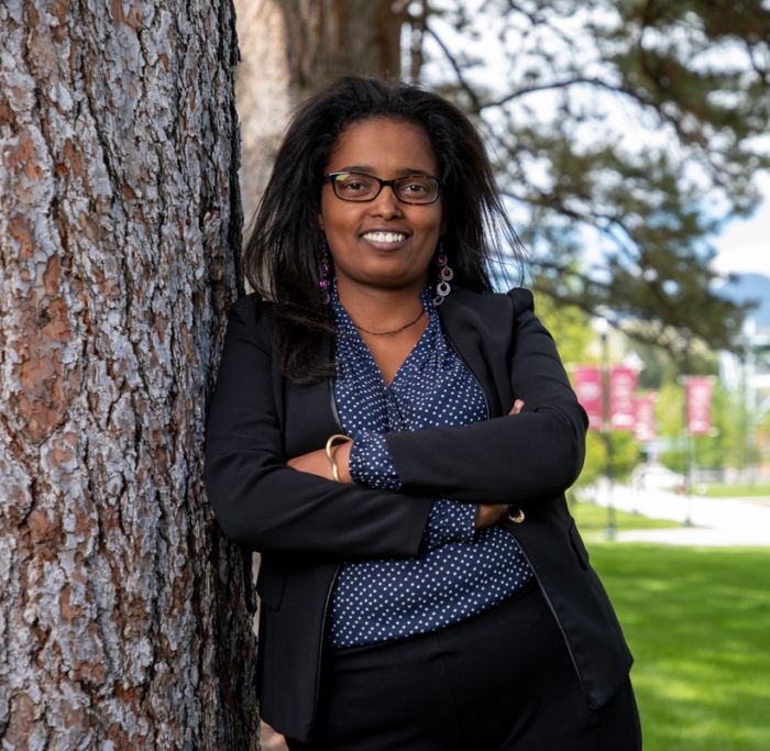 Doctoral student Hana Meshesha leans against a tree outside the Education Building and smiles at the camera.