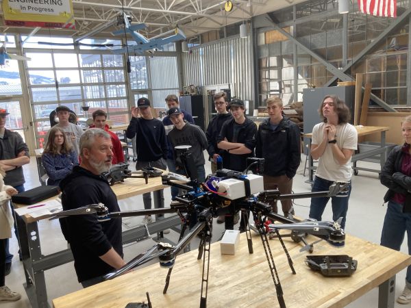 students listening to a professor talk about a drone in the center of the class