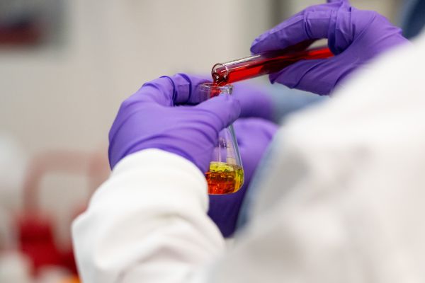 Lab tech pouring red liquid into a beaker.