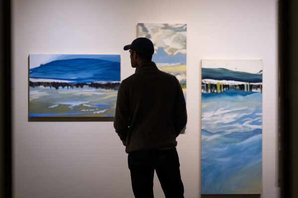 A lone figure stands in front of a UC Gallery wall with art displayed