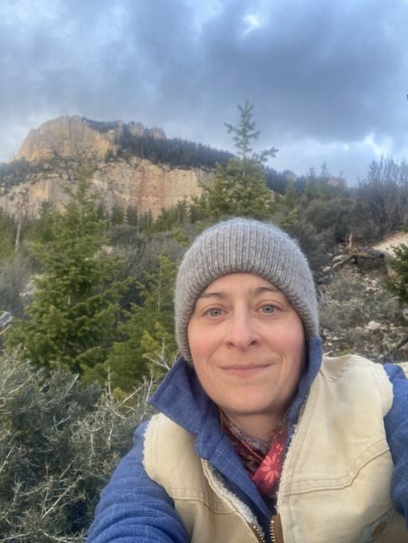 Kay Hajek smiles, posing in front of a mountain on an overcast day.