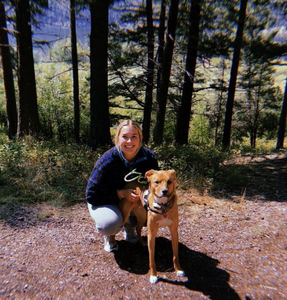 Grace Bintz in a forest crouching next to her dog