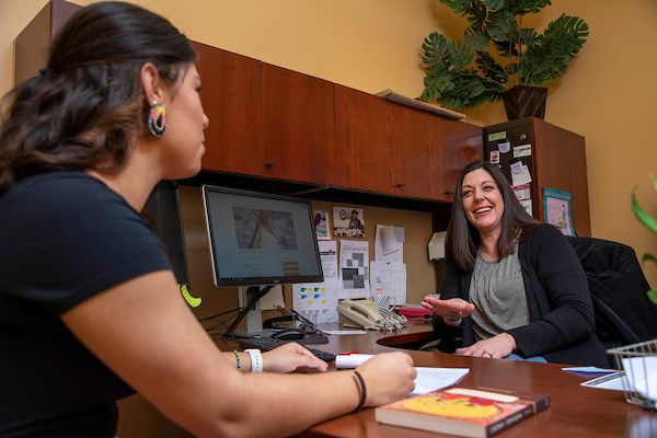 two women sit across a desk and speak