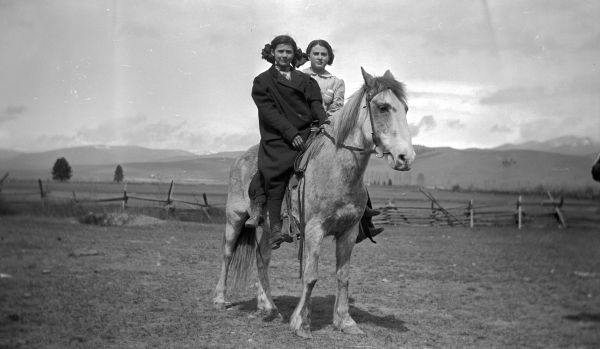 Two girls on horseback near a school