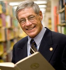 George Dennison reading a book in the Mansfield Library stacks